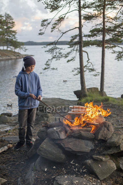 Garçon faisant feu de joie par le lac Harsjon au coucher du soleil — Photo de stock