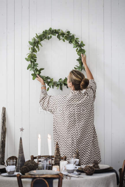 Woman hanging Christmas wreath on wall — Stock Photo
