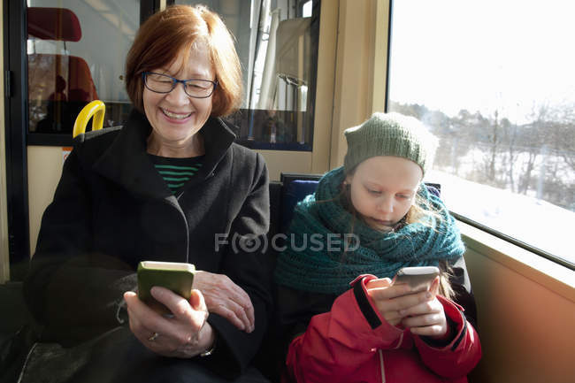 Девушка с бабушкой сидит в трамвае и пользуется смартфонами — стоковое фото