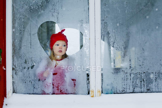 Girl looking through frosted window — Stock Photo