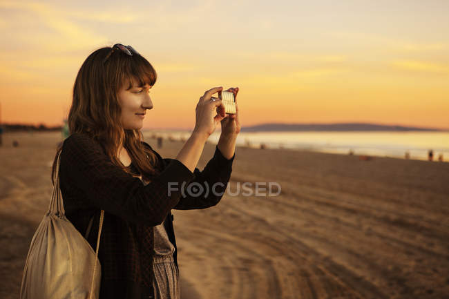 Середня доросла жінка фотографується на заході сонця — стокове фото