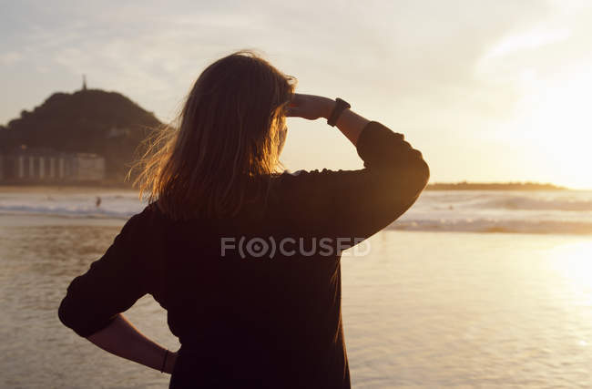 Женщина, стоящая на пляже и смотрящая на Бискайский залив на закате — стоковое фото