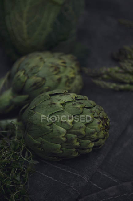 Fresh green artichokes and thyme on tablecloth — Stock Photo