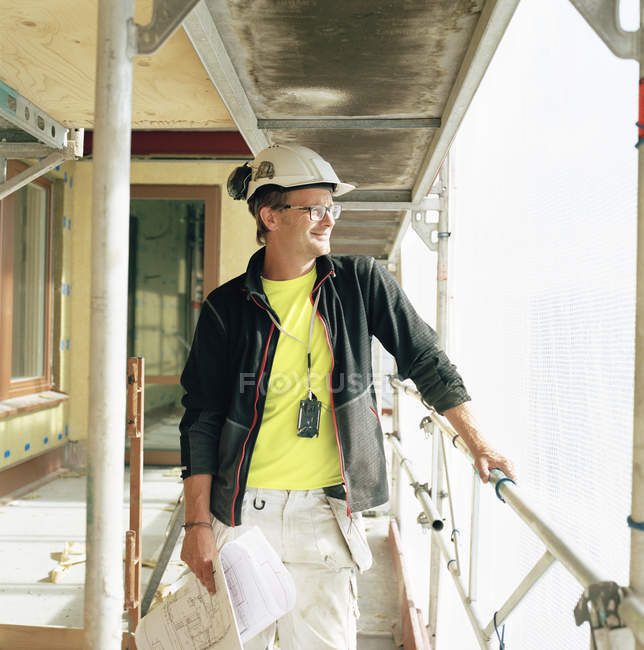 Trabajador de la construcción sosteniendo planos y mirando hacia otro lado - foto de stock