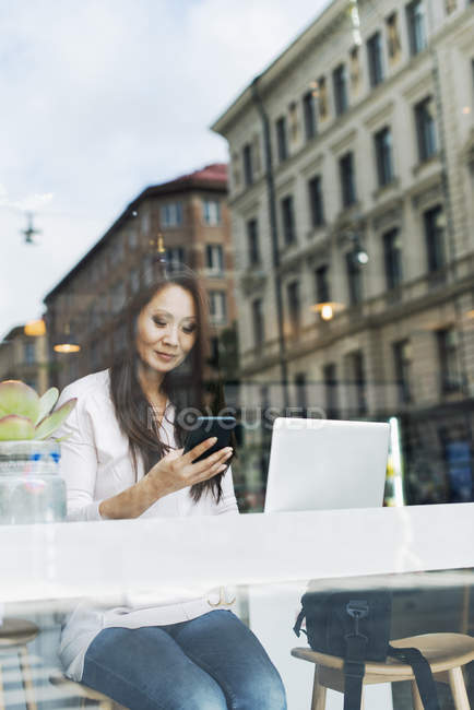 Mujer usando teléfono inteligente, vista desde la ventana - foto de stock