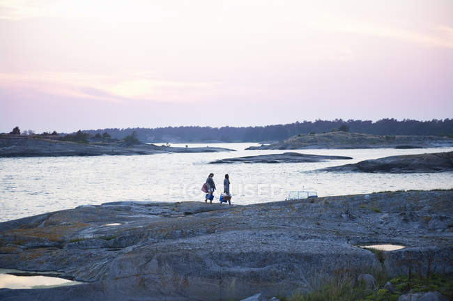 Vista lateral de dos mujeres caminando sobre rocas a lo largo del mar - foto de stock