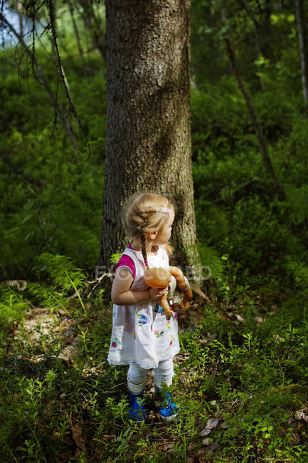 Chica con muñeca de pie delante del árbol - foto de stock