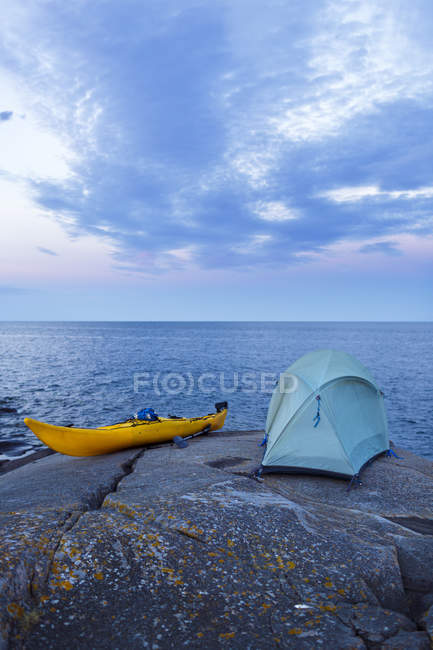 Caiaque e tenda na rocha à beira-mar ao entardecer — Fotografia de Stock