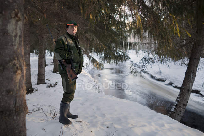 Hunter de pé na margem do rio nevado e olhando para longe — Fotografia de Stock