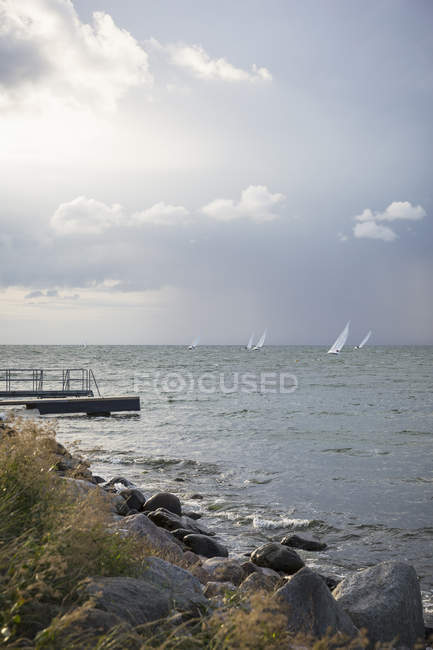 Rocky river shore with sailboats on water — Stock Photo