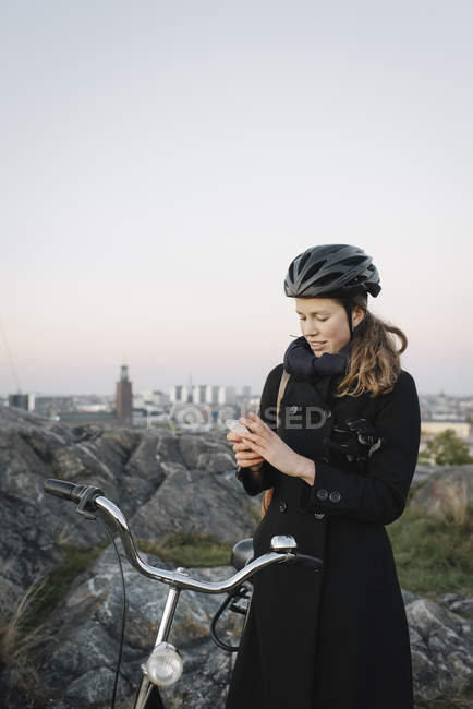 Mujer joven de pie en bicicleta y el uso de teléfono, se centran en primer plano - foto de stock