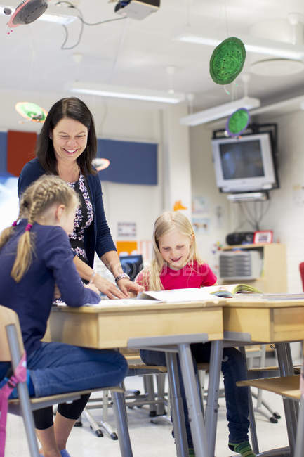 Girls and teacher smiling in classroom, focus on foreground — Stock Photo