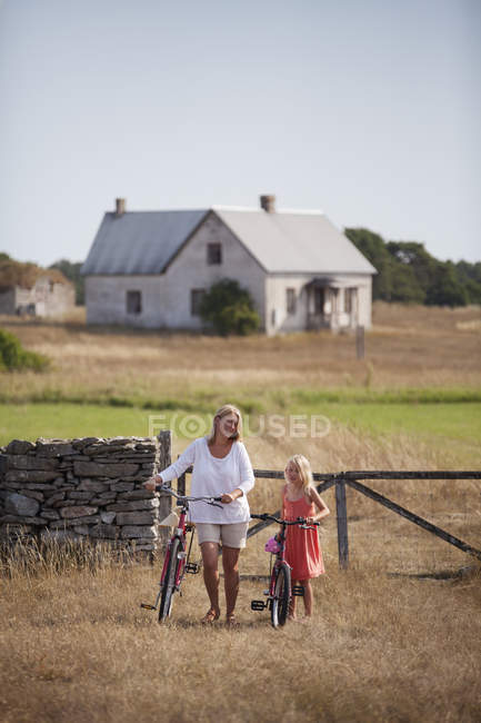 Mother and daughter wheeling bicycles at farm, differential focus — Stock Photo