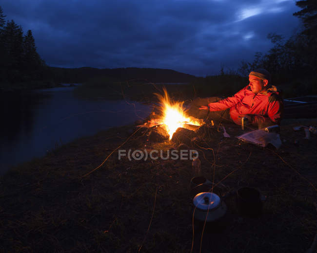 Homme par feu de joie au bord de la rivière, foyer sélectif — Photo de stock