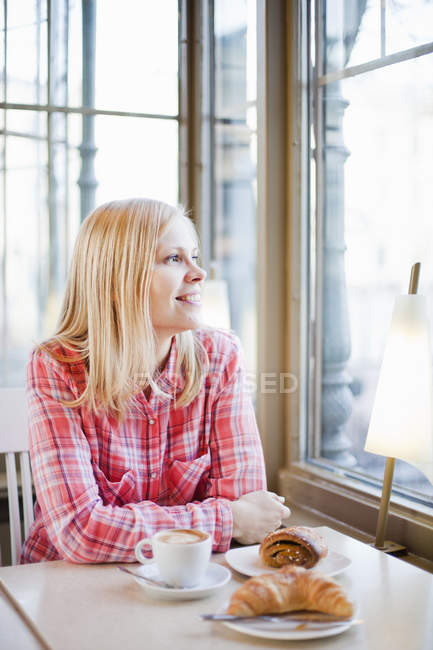Femme regardant par la fenêtre du café et souriant — Photo de stock