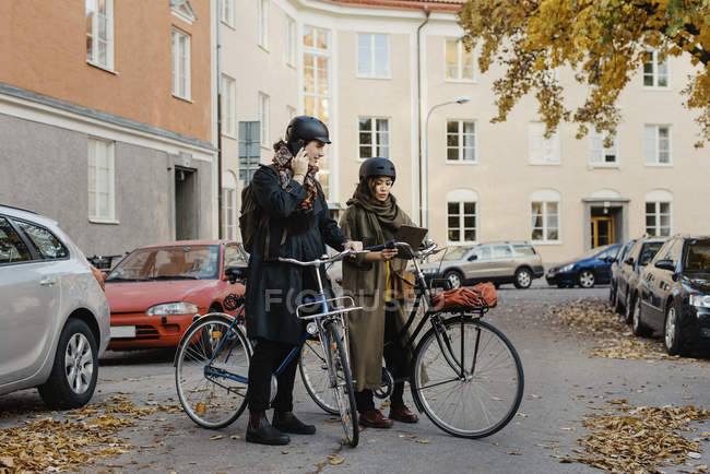 Pareja de pie con bicicletas, mujer usando tableta digital, enfoque selectivo - foto de stock