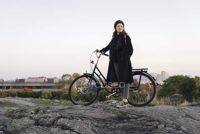 Vue latérale de la jeune femme debout à vélo sur le rocher — Photo de stock