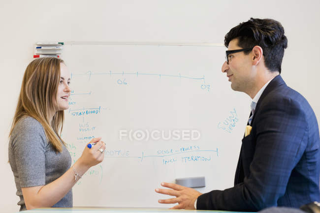Side view of business people talking in front of whiteboard — Stock Photo