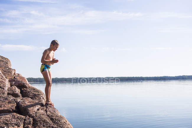 Garçon debout sur le rocher et regardant l'eau — Photo de stock