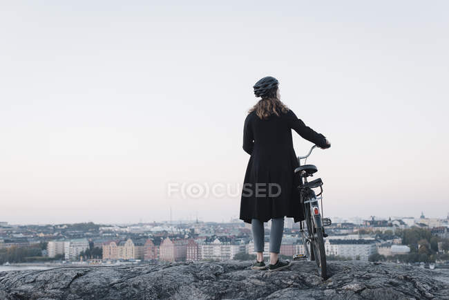 Visão traseira da jovem mulher de pé de bicicleta na rocha — Fotografia de Stock