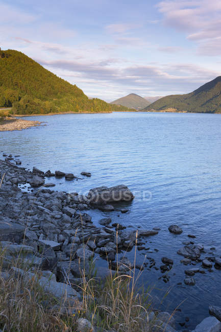 Rocky river shore and sun lighted mountains — Stock Photo