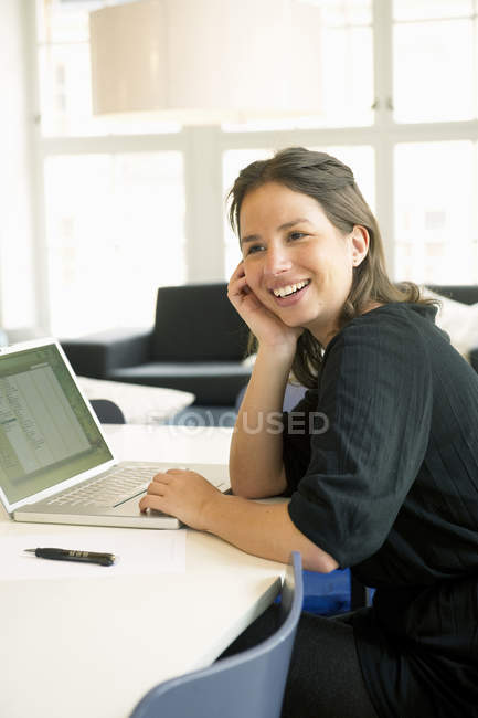 Retrato de mujer joven usando laptop y sonriendo - foto de stock