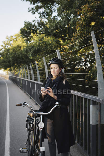 Giovane donna in piedi in bicicletta e utilizzando il telefono — Foto stock