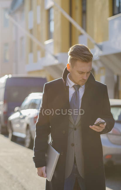 Uomo d'affari sms in strada illuminata dal sole, concentrarsi sul primo piano — Foto stock