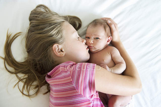 Высокий угол зрения девочки, лежащей на кровати с новорожденной сестрой — стоковое фото