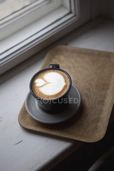 Placa de madeira com xícara de latte no peitoril da janela — Fotografia de Stock