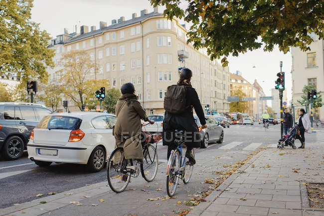 Rear view of man and woman cycling on city street — Stock Photo