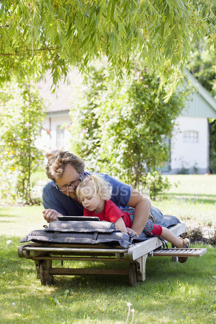 Дочь с отцом лежит на шезлонге и с помощью планшетного ПК — стоковое фото