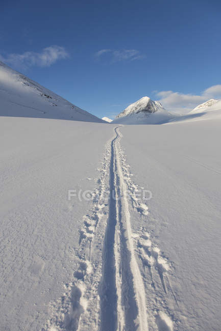 Ski trails on snow with mountains under blue sky — Stock Photo