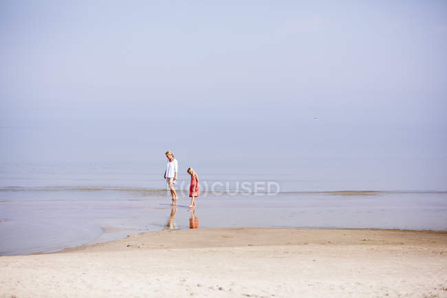 Вид сбоку на мать и дочь, стоящие на отмелях пляжа — стоковое фото