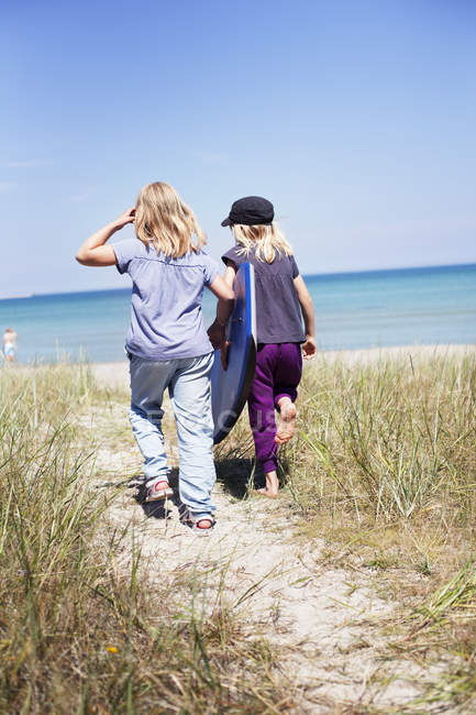 Deux filles marchent sur la plage au soleil — Photo de stock