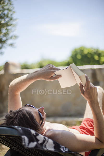 Чоловік засмагає і читає книгу, фокус на передньому плані — стокове фото