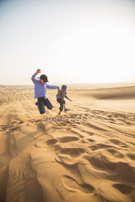 Dos chicos saltando sobre la arena en el desierto, enfoque selectivo - foto de stock
