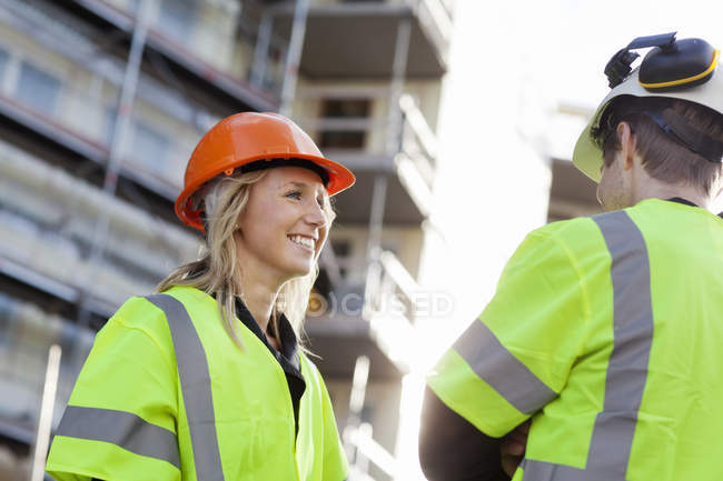 Zwei Personen stehen sich in Schutzhelmen und reflektierender Kleidung auf Baustelle gegenüber — Stockfoto