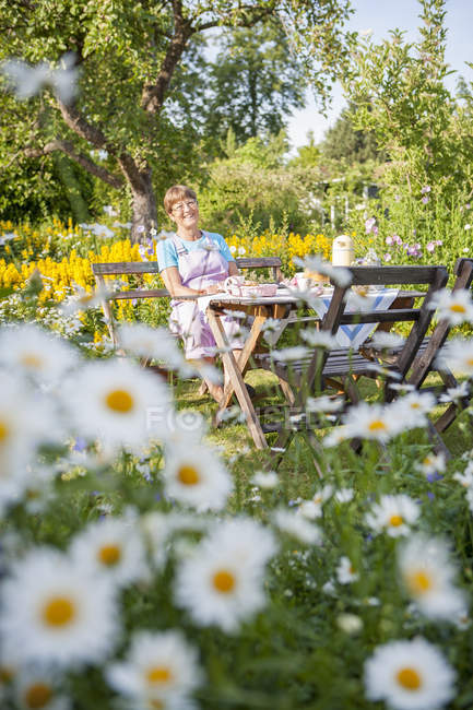 Жінка розслабляється за столом в освітленому сонцем саду — стокове фото