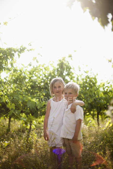 Porträt einer Schwester, die ihren jüngeren Bruder im Obstgarten umarmt — Stockfoto