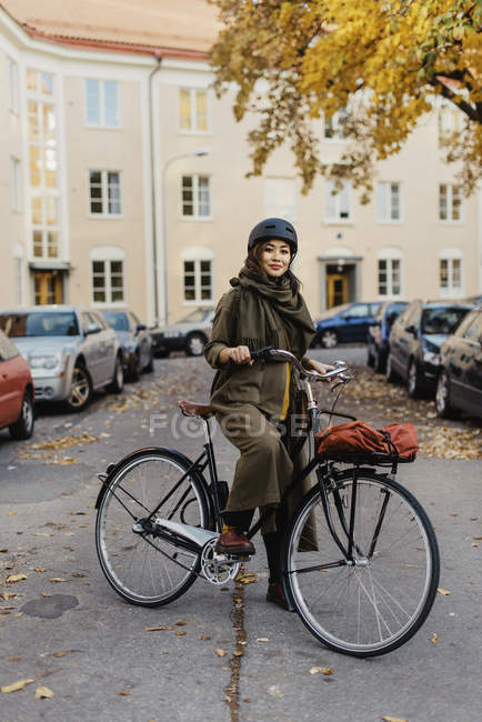 Mujer joven de pie con bicicleta contra la calle - foto de stock