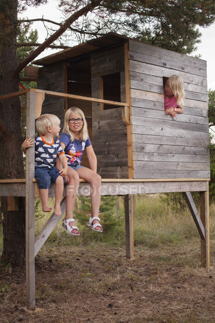 Брат з сестрами, сидячи на ганку дерев'яного будинку — стокове фото