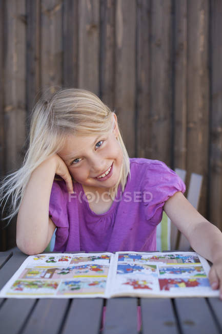 Menina com quadrinhos à mesa ao ar livre, foco diferencial — Fotografia de Stock