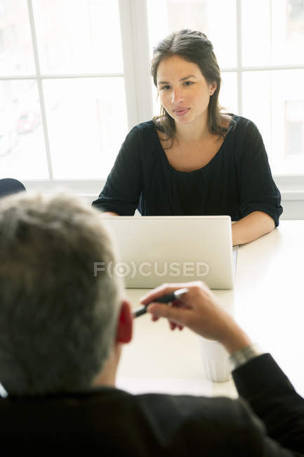 Young woman and mature man sitting at desk in office — Stock Photo
