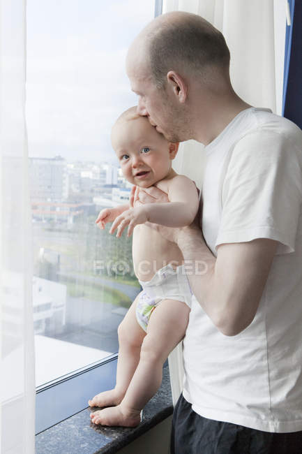 Pai com bebê filho olhando através da janela em casa — Fotografia de Stock