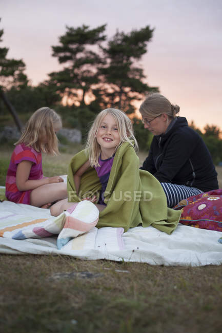 Menina sentada no cobertor de piquenique com mãe e irmã, foco em primeiro plano — Fotografia de Stock