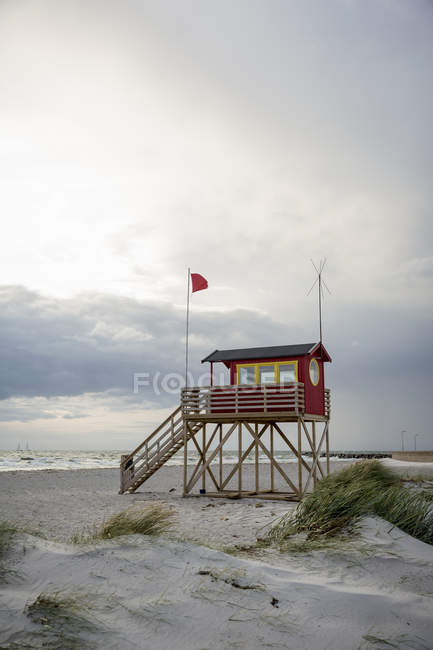 Cabane de sauveteur rouge sur la plage avec ciel couvert — Photo de stock