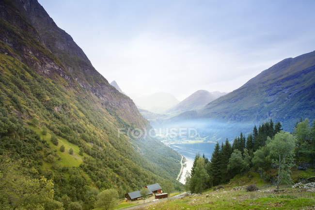 Small houses by green mountains with low clouds — Stock Photo