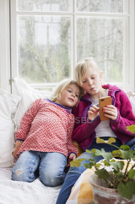 Irmãs usando telefone inteligente em casa, foco seletivo — Fotografia de Stock