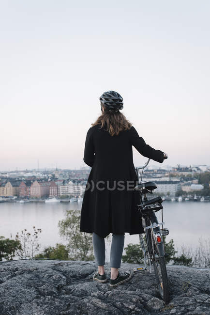 Rear view of young woman standing by bicycle on rock — Stock Photo